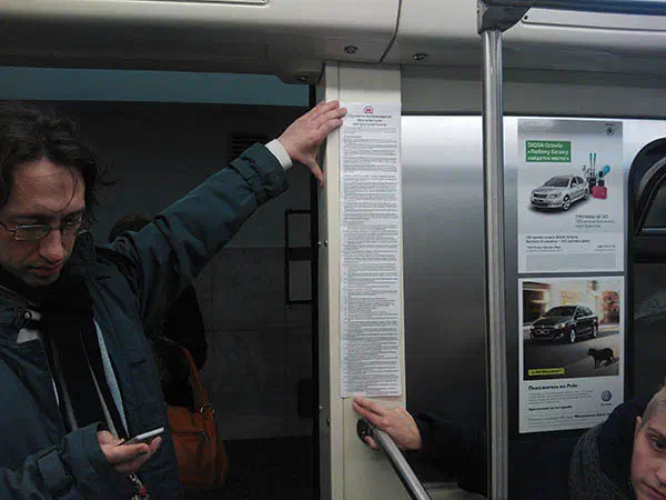 Изображается мужчина, стоящий на поезде метро, держащий телефон в одной руке и бумагу в другой.