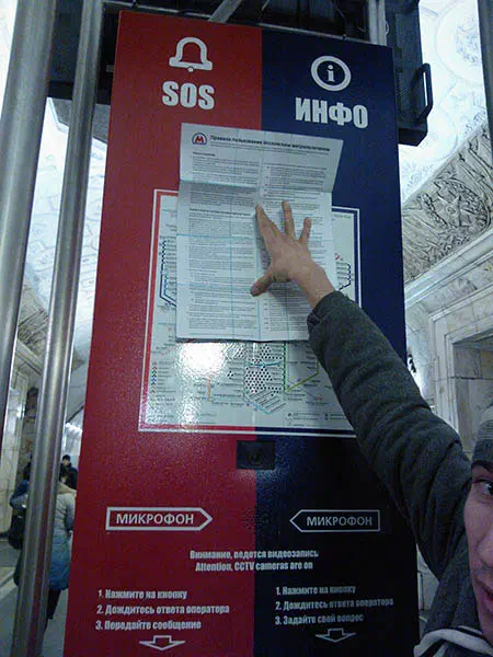 Изображение показывает мужчину, указывающего на знак на стороне поезда. Он стоит перед доской с текстом на ней, и на заднем плане несколько человек.