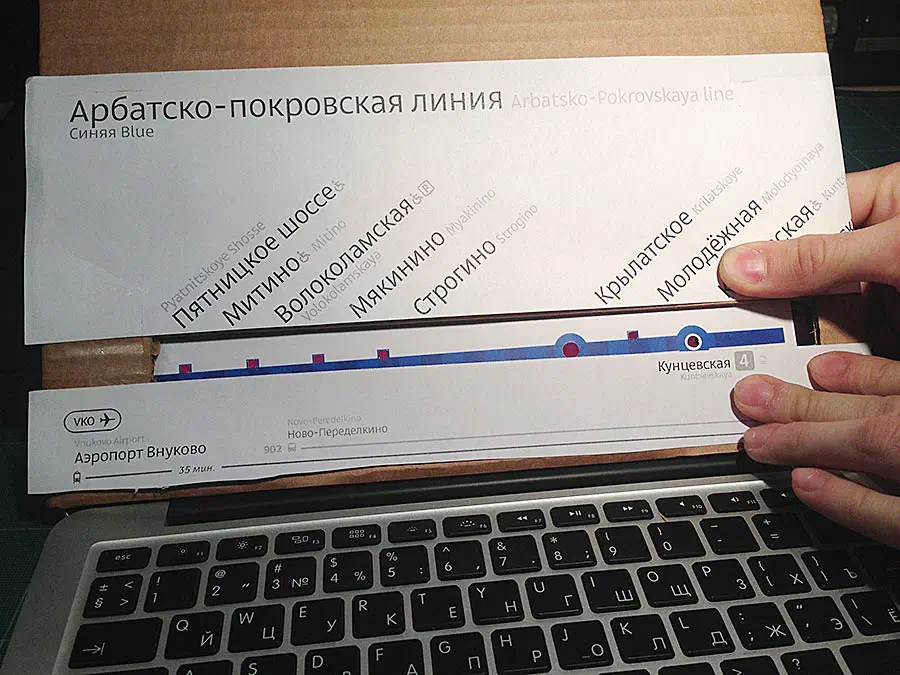 На снимке изображен человек, держащий клочок бумаги перед ноутбуком на столе. Рука человека видна с правой стороны изображения, ноутбук открыт и бумага кажется