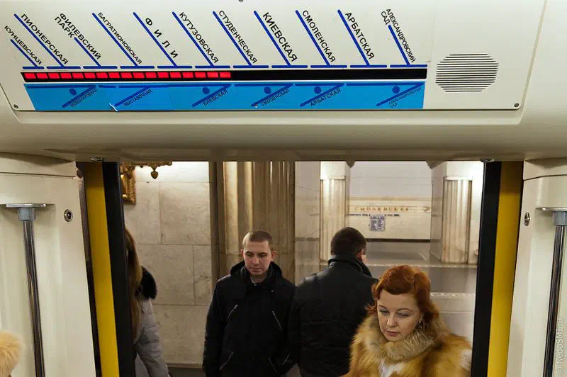 Изображение показывает группу людей, стоящих на вершине поезда метро в Москве, Россия. Внутри поезда полно людей, на заднем плане есть стена. На верхнем этаже.