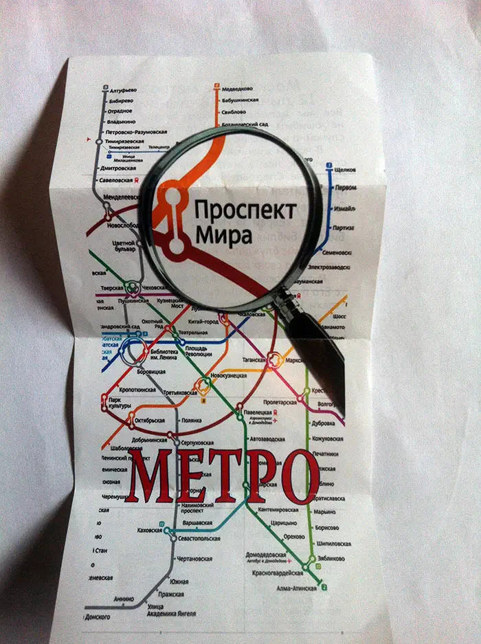 Изображение показывает увеличительное стекло, зависающее над бумагой с картой московской системы метро. Бумага белая, а карта детализирована, показывая различные линии и станции системы метро.