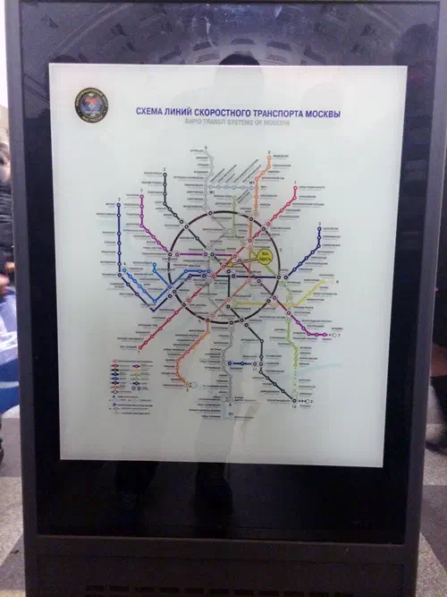 Карта показывает карту московской системы Метро в стеклянном ящике, где несколько человек стоят слева от нее.