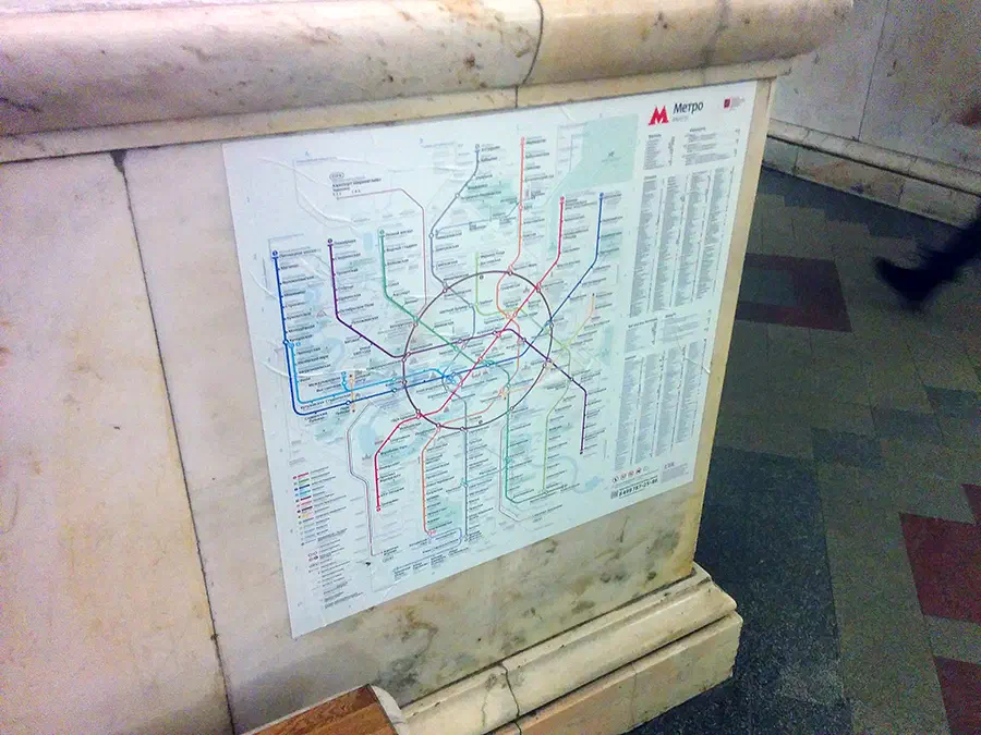 На снимке изображен плакат на стене станции метро с картой на ней, и нога человека, видимая с правой стороны изображения.