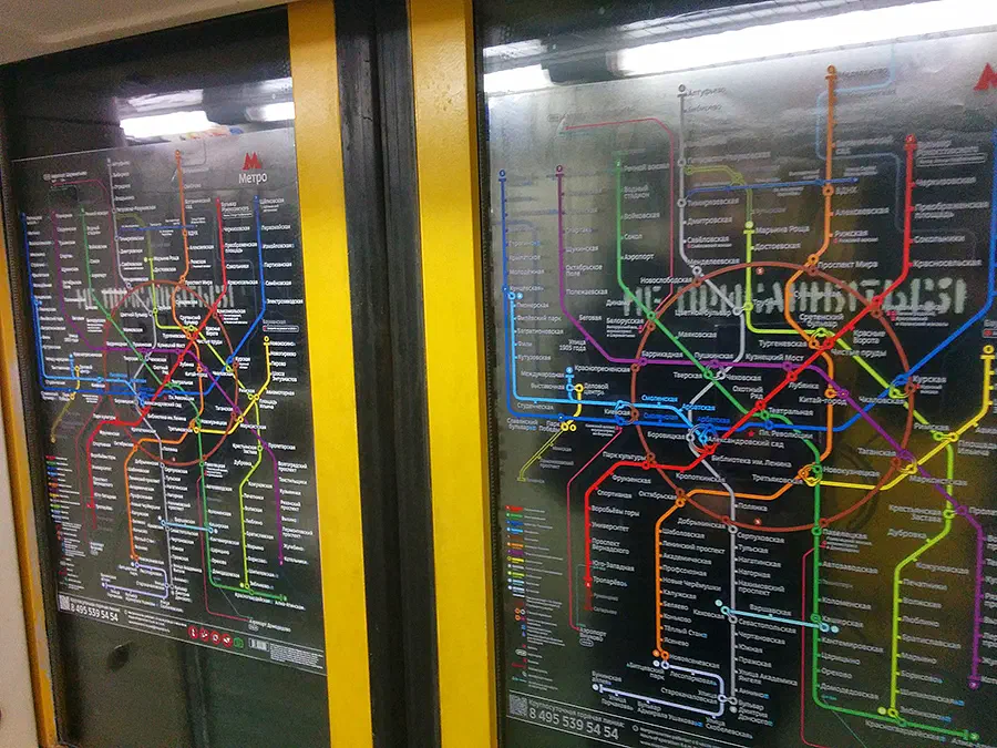 Карта показывает карту метро на станции метро Москвы. Карта освещена огнями наверху изображения, и на заднем плане есть две двери.