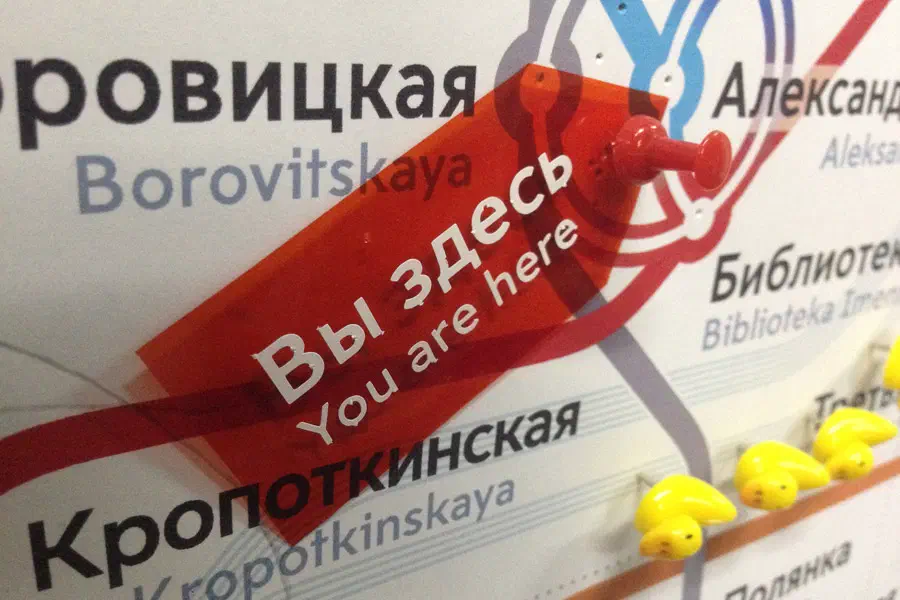 На рисунке показана постер с текстом на нём и куча желтых резиновых уток, сидящих сверху. Текст на плакате гласит: "Ты здесь", и на стене есть красный объект.