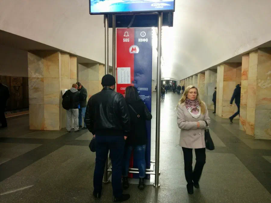 На рисунке изображена группа людей, стоящих на станции метро рядом друг с другом, несколько человек ходят по полу и несколько столбов по обе стороны.