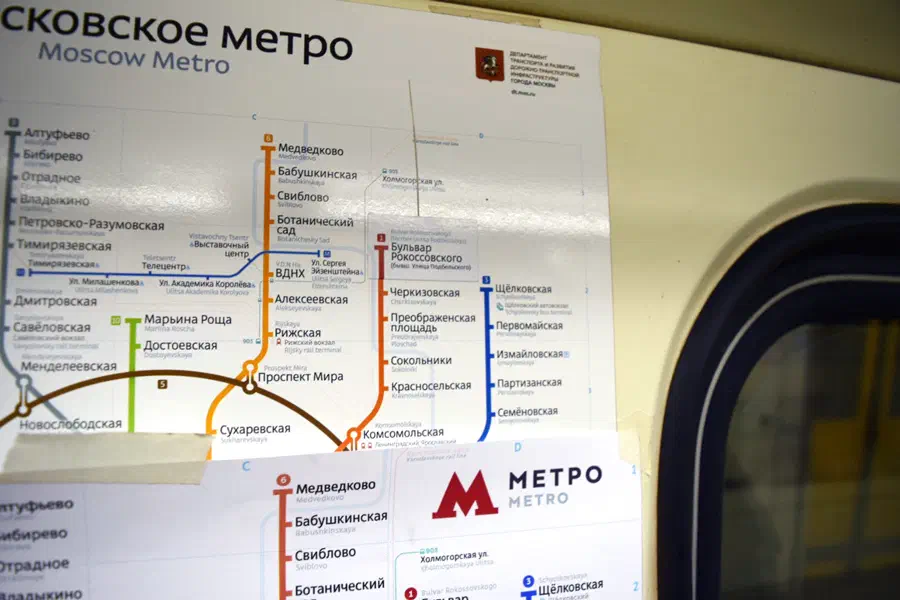 Изображение показывает плакат на стене станции метро в Москве, Россия, с картой московской системы метро. Окно поезда видно с правой стороны изображения.