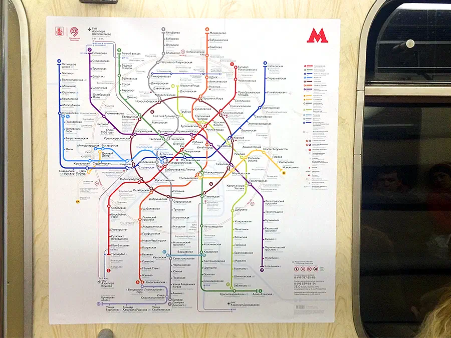 На снимке изображен плакат с картой московской системы метро на деревянной стене с стеклянным окном с правой стороны и несколькими людьми, видимыми через окно.